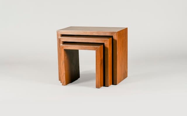 A nesting set of oak side tables on a plain studio backdrop.